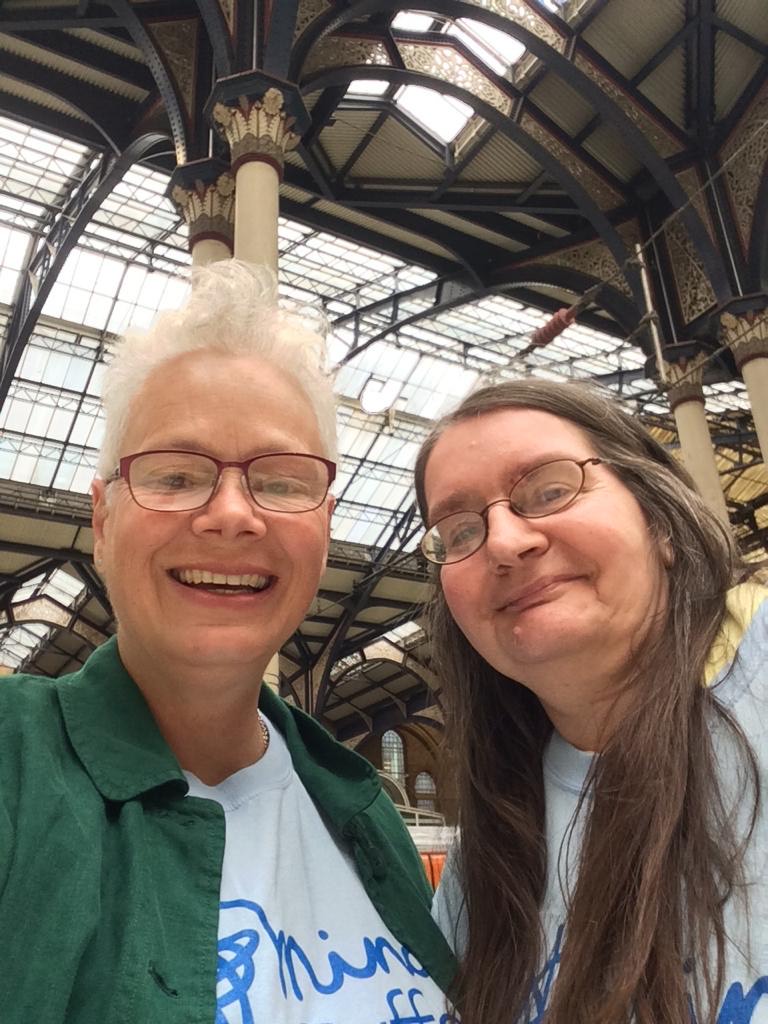 Two people smiling after arriving at a station. Sharon our GreenCare gardener overcomes anxiety to meet Sarah in London for the Chelsea Flower Show.