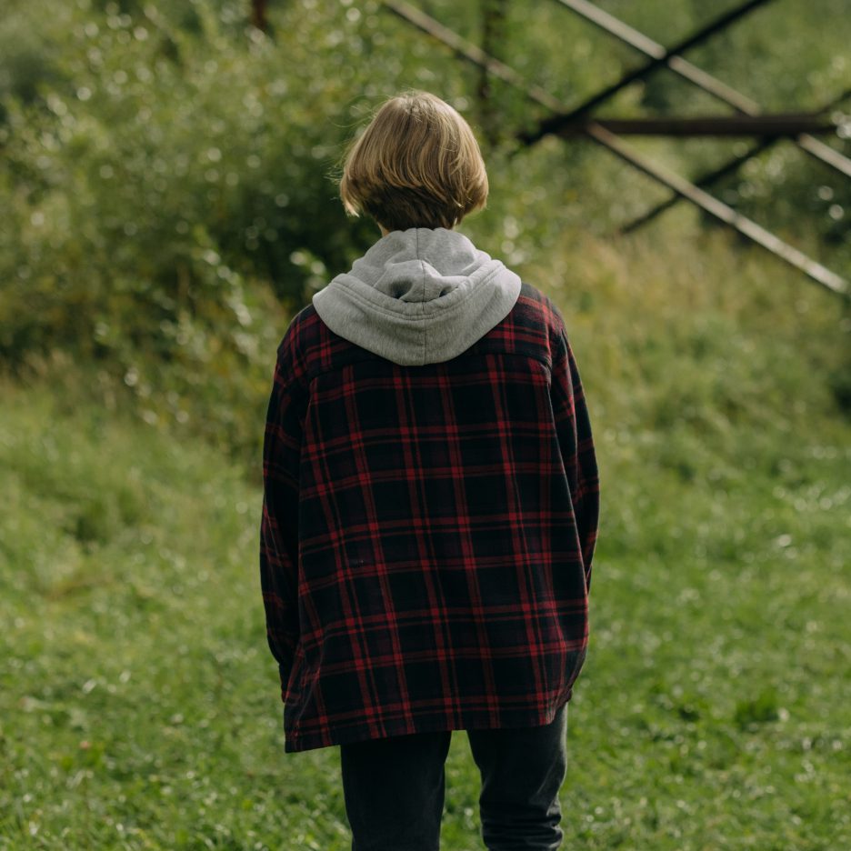 A person stands in a garden or meadow looking out into the grass, with their back to the camera.