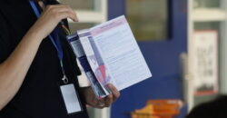 A person in a classroom holds up an open booklet, the header of the page says 'Need support?'