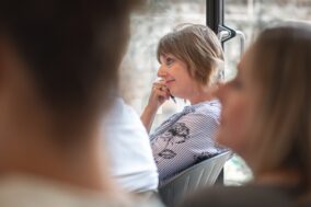 People sitting down in a training setting, listening to a speaker who is out of shot. A woman rests her head on her hands as she pays attention.
