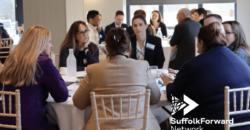 A group of people sit around a table talking in a corporate networking setting.